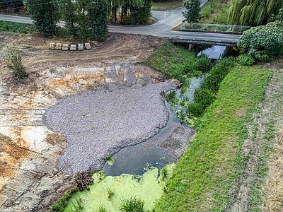 Luftaufnahme von der Baustelle mit Steinen, Kiesfläche und Gewässer.
